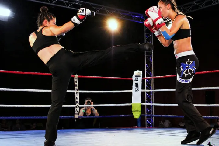 Sur le ring d’un gala, une tireuse lance un coup de pied haut face à une boxeuse du TCMS en garde.